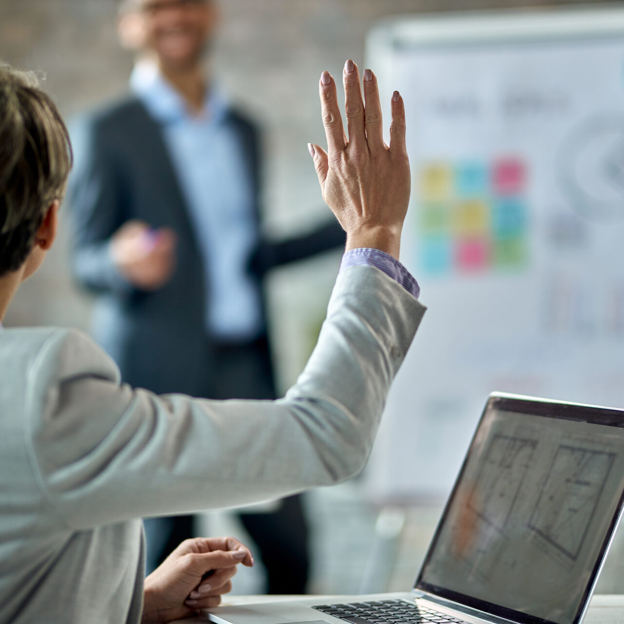 Back view of female entrepreneur raising  hand to answer the question during business presentation in the office.